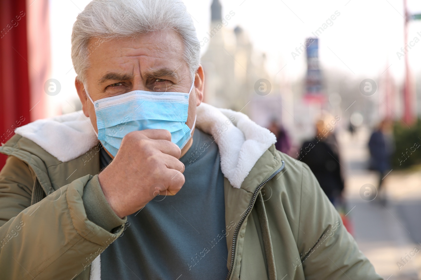 Photo of Senior man with medical mask coughing on city street. Virus protection