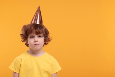 Photo of Upset little boy in party hat on orange background. Space for text