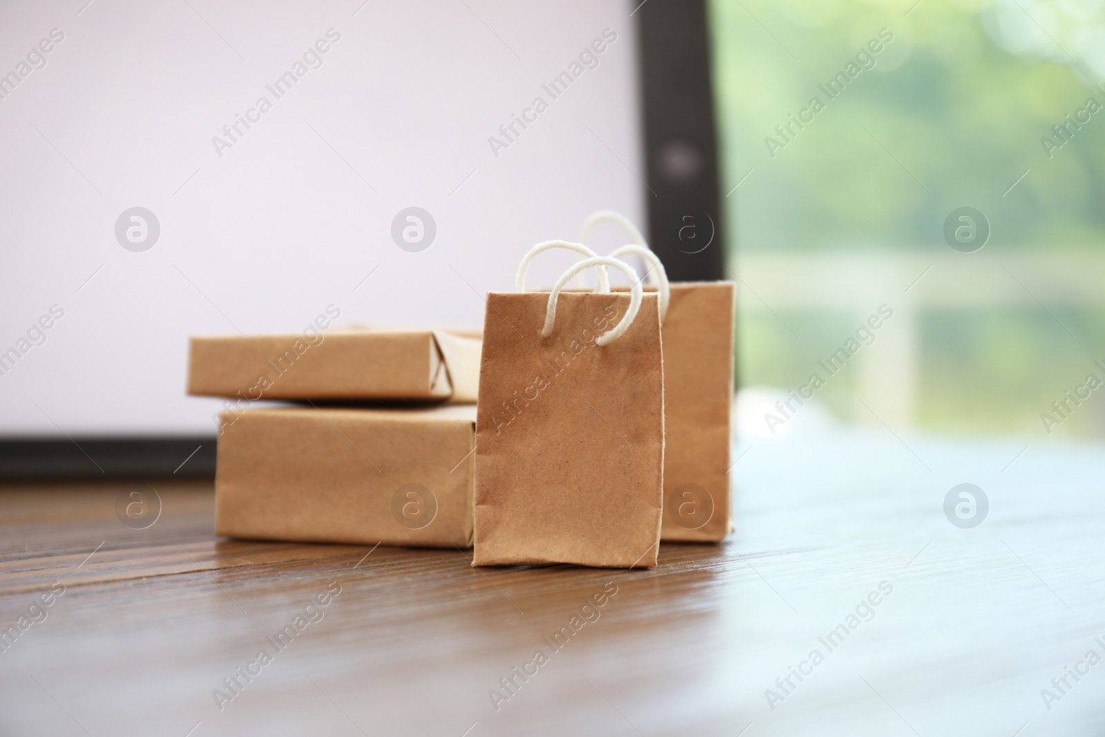 Photo of Internet shopping. Small bags and boxes near modern tablet on table indoors, closeup