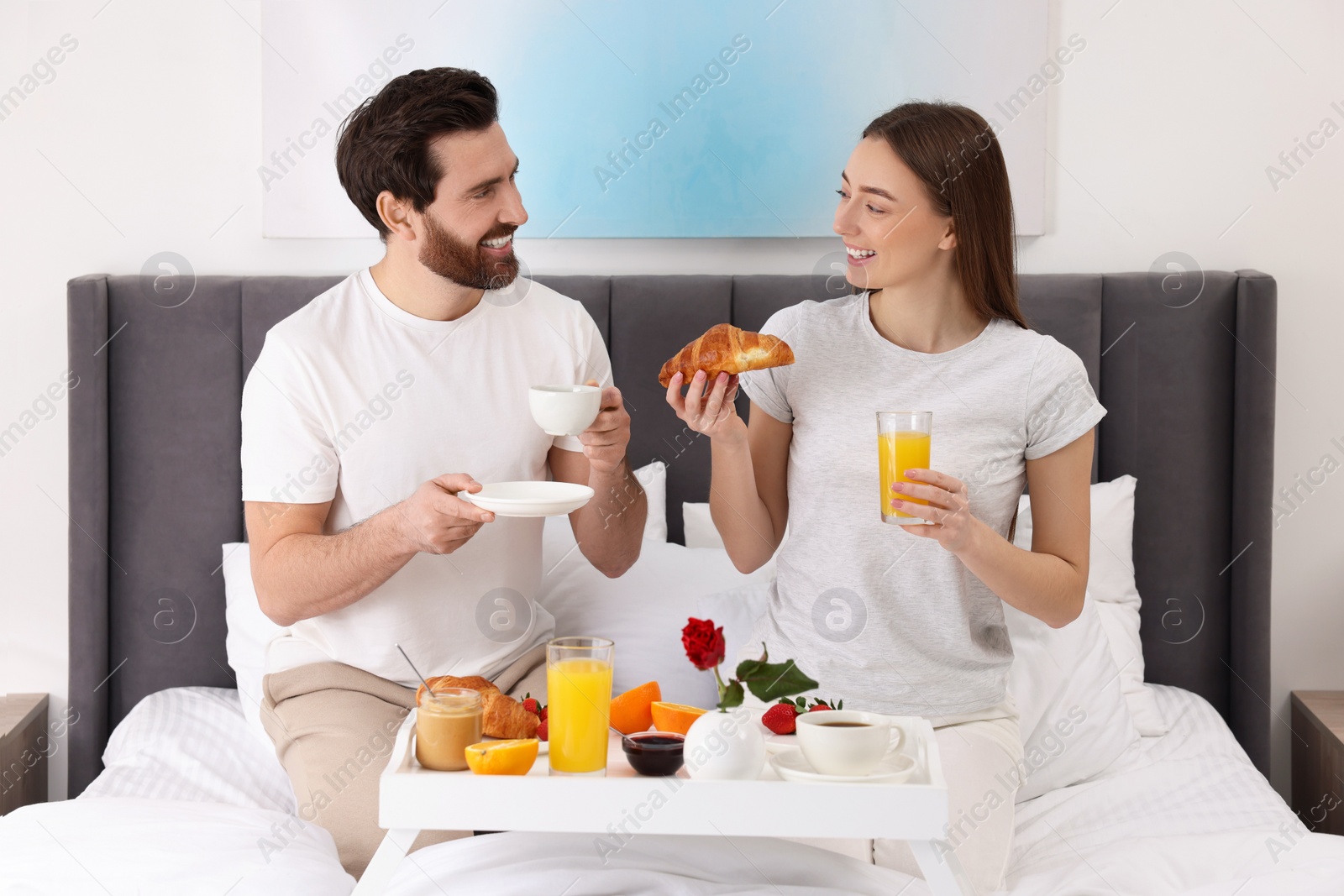 Photo of Happy couple having breakfast and talking on bed at home