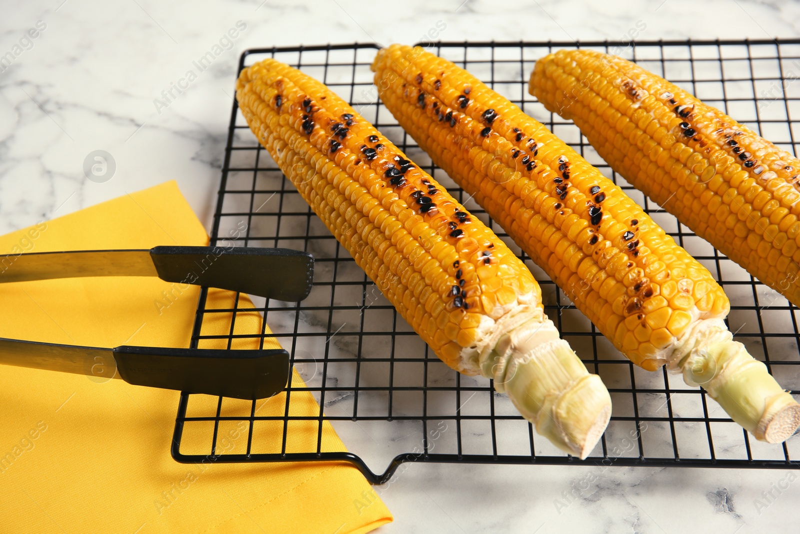 Photo of Cooling rack with grilled corn cobs on marble background