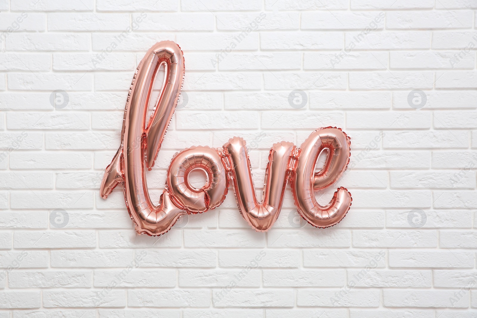 Photo of Pink foil balloon in shape of word Love on white brick wall. Valentine Day celebration