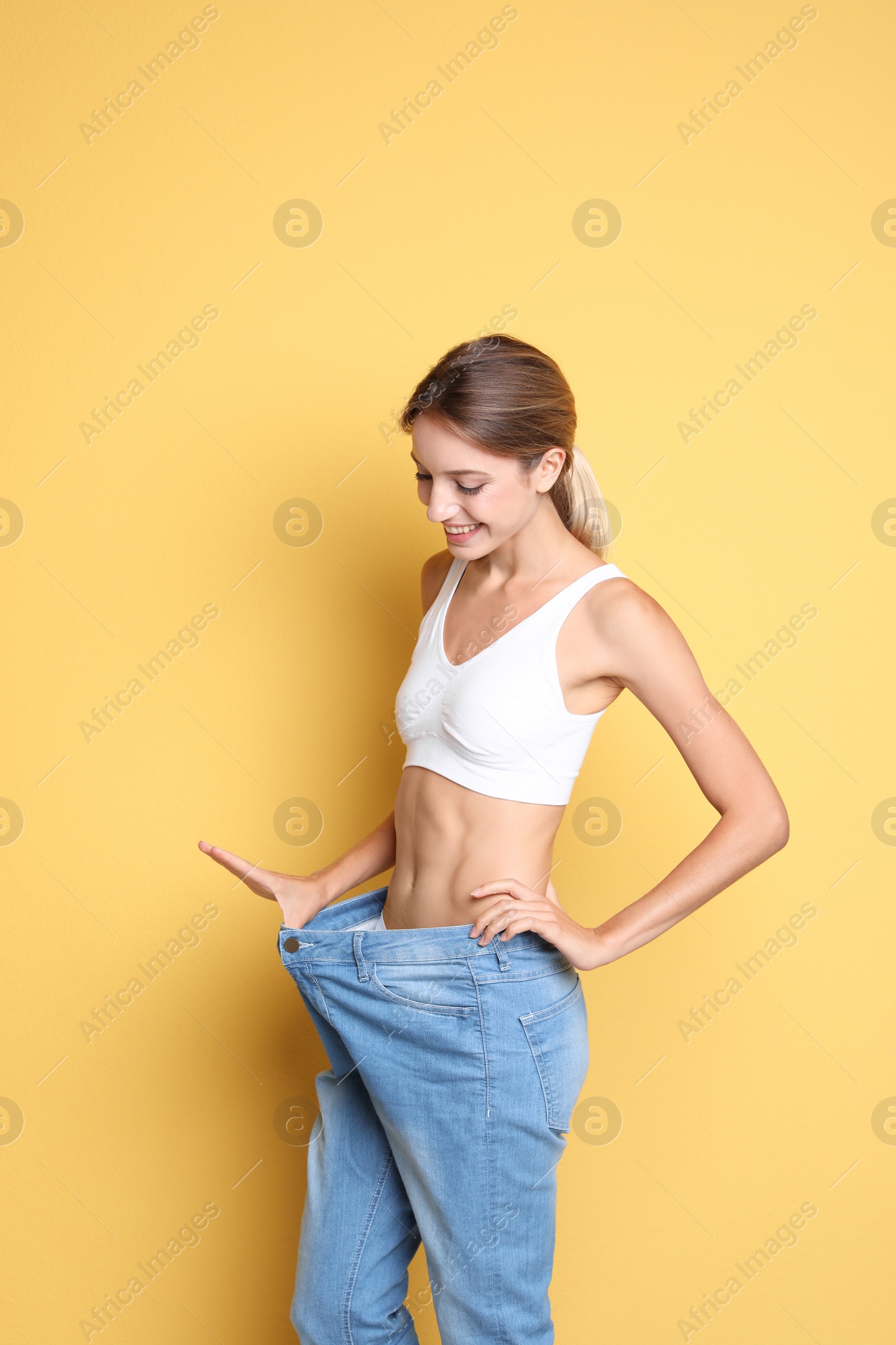 Photo of Young slim woman in old big jeans showing her diet results on color background