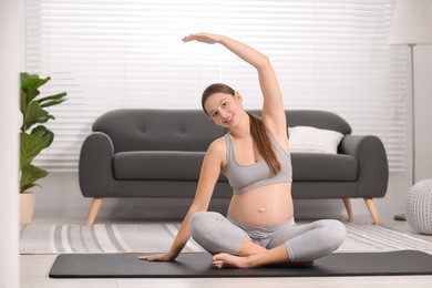 Photo of Pregnant woman doing exercises on yoga mat at home