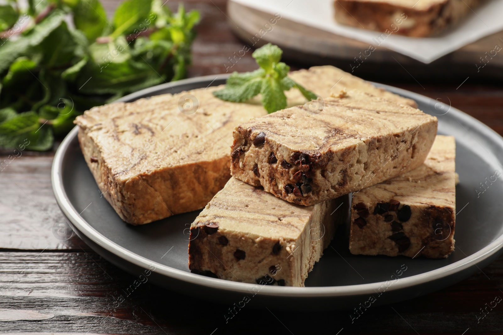 Photo of Pieces of tasty chocolate halva with mint on wooden table, closeup