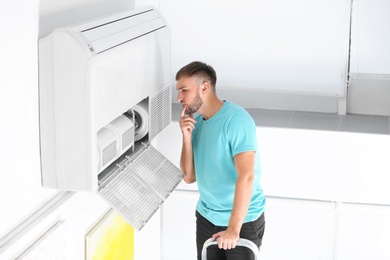 Young man fixing air conditioner at home