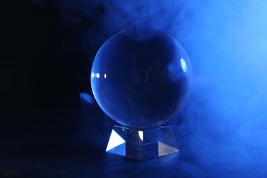 Photo of Magic crystal ball on table and smoke against dark background. Making predictions