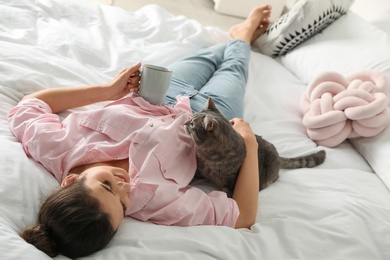 Young woman with cute cat on bed at home. Pet and owner