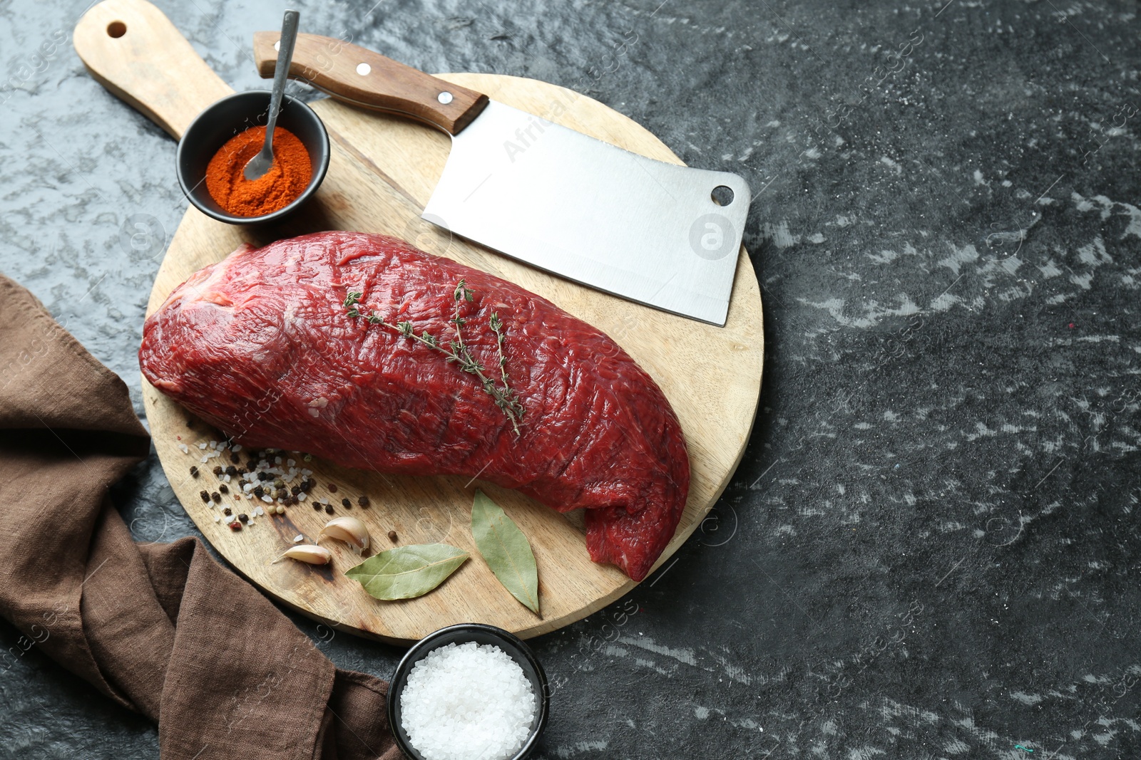 Photo of Piece of raw beef meat, knife and spices on black textured table, above view. Space for text