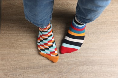 Man in different stylish socks standing on wooden floor, top view