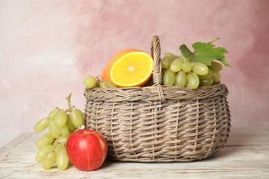 Photo of Wicker basket with different fruits on white wooden table near pink wall