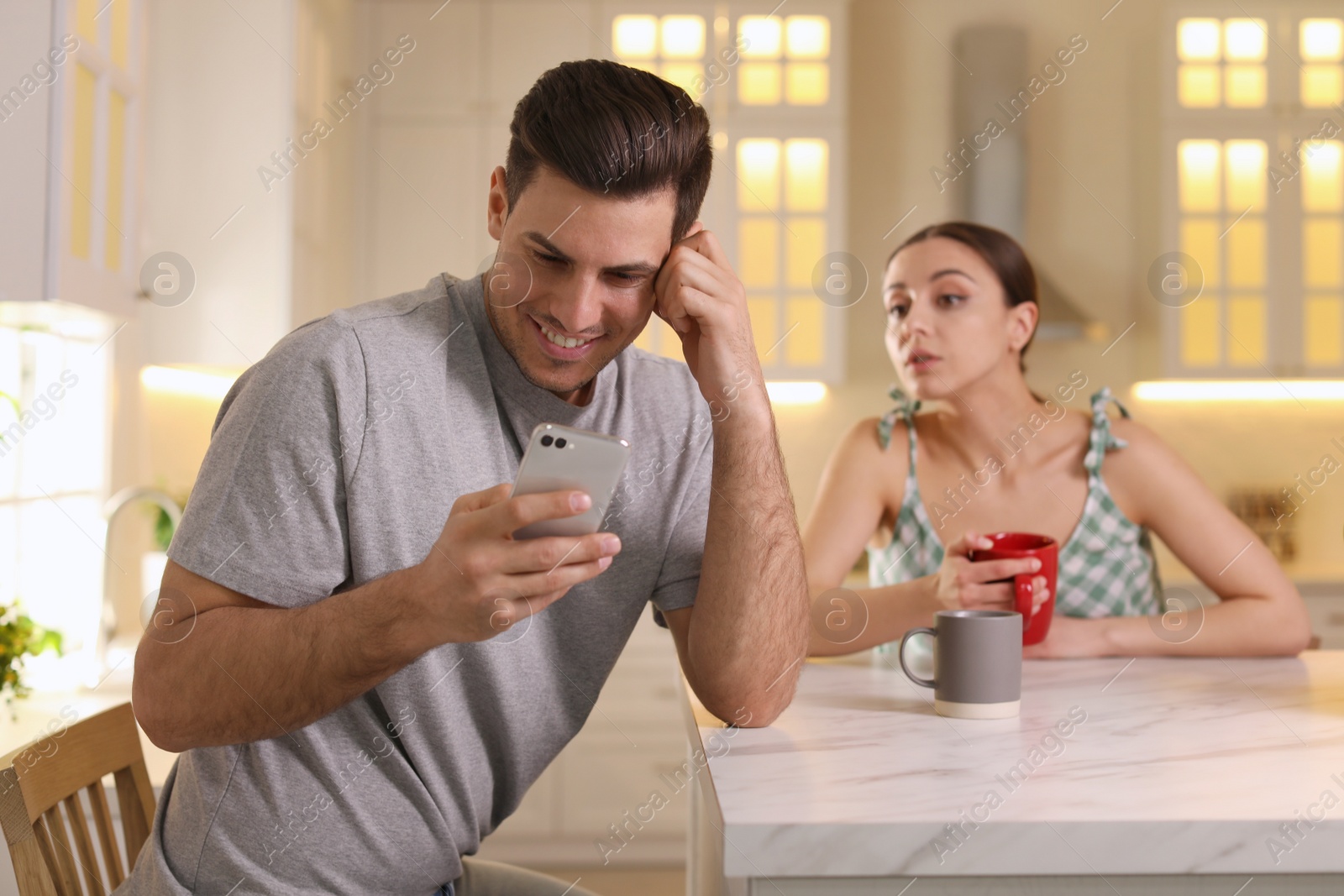 Photo of Distrustful woman peering into boyfriend's smartphone at home. Jealousy in relationship