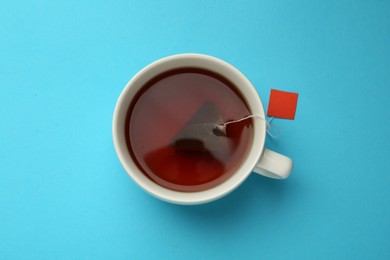 Photo of Tea bag in cuphot water on light blue background, top view