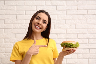 Young woman with tasty burger near brick wall. Space for text