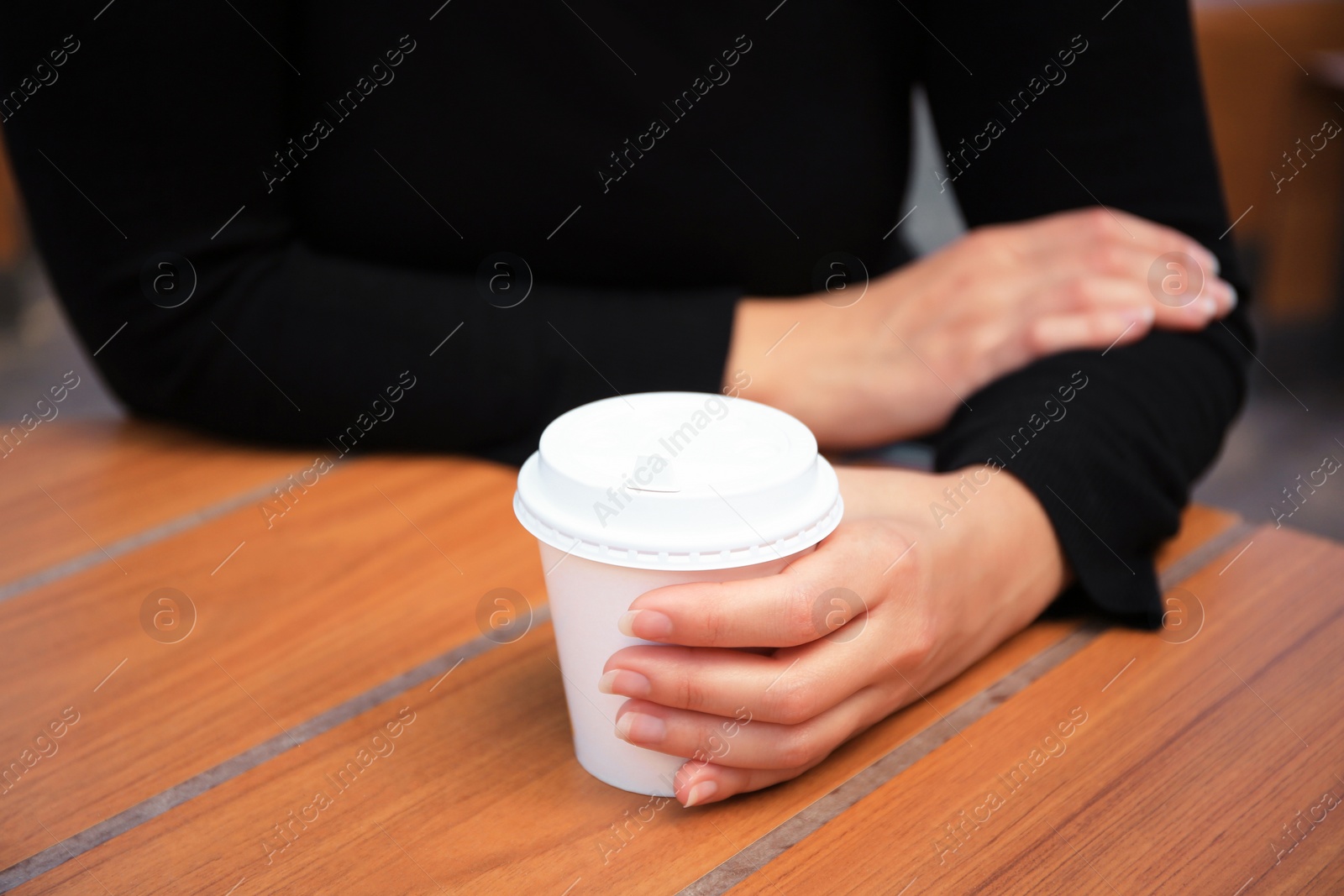 Photo of Woman with cardboard cup of coffee at table, closeup