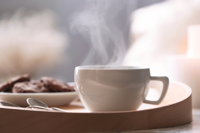 Cup of hot drink on wooden tray against blurred background, closeup