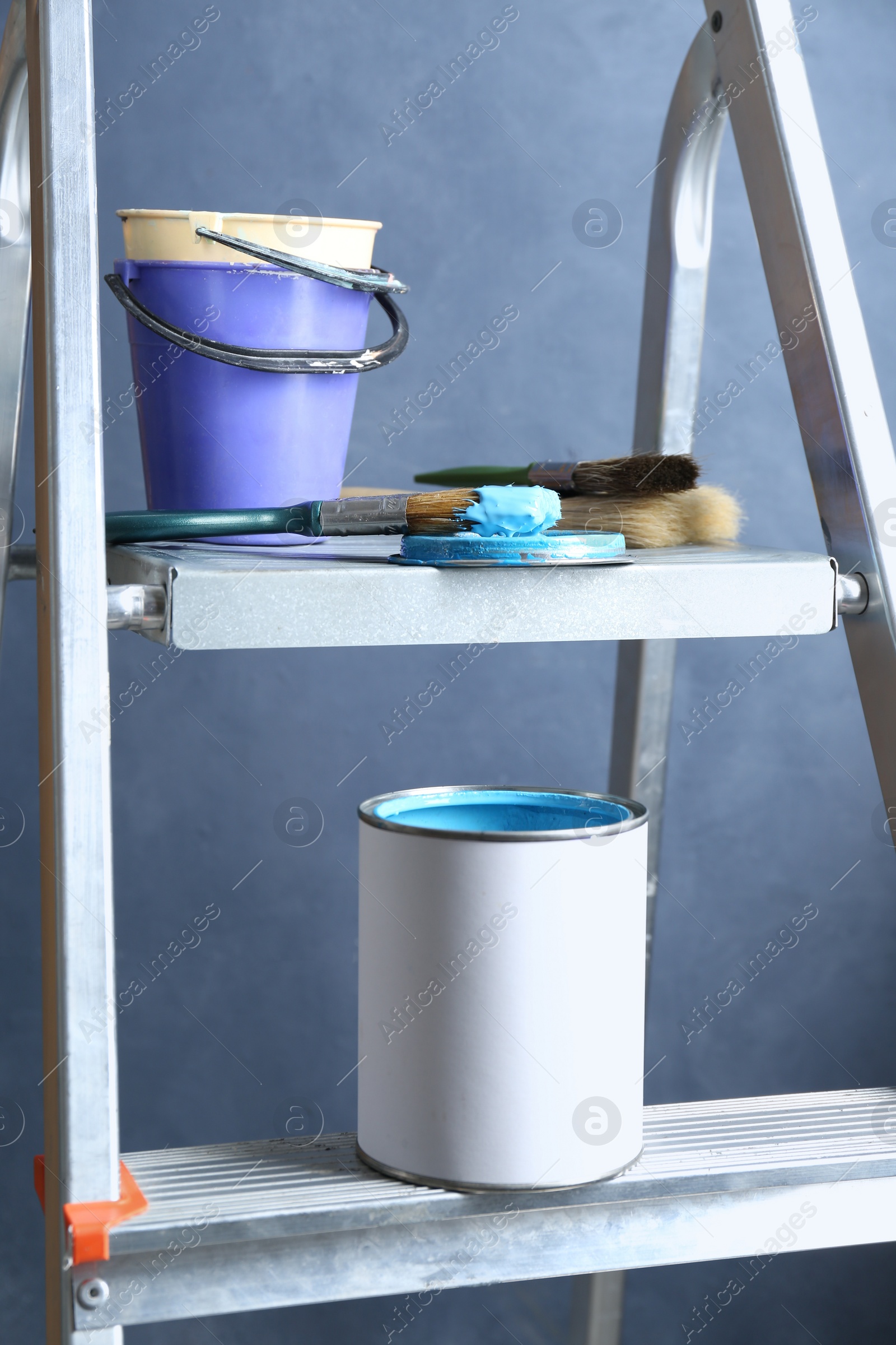 Photo of Can of light blue paint, brushes and buckets on metal ladder