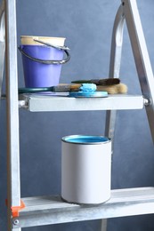 Photo of Can of light blue paint, brushes and buckets on metal ladder