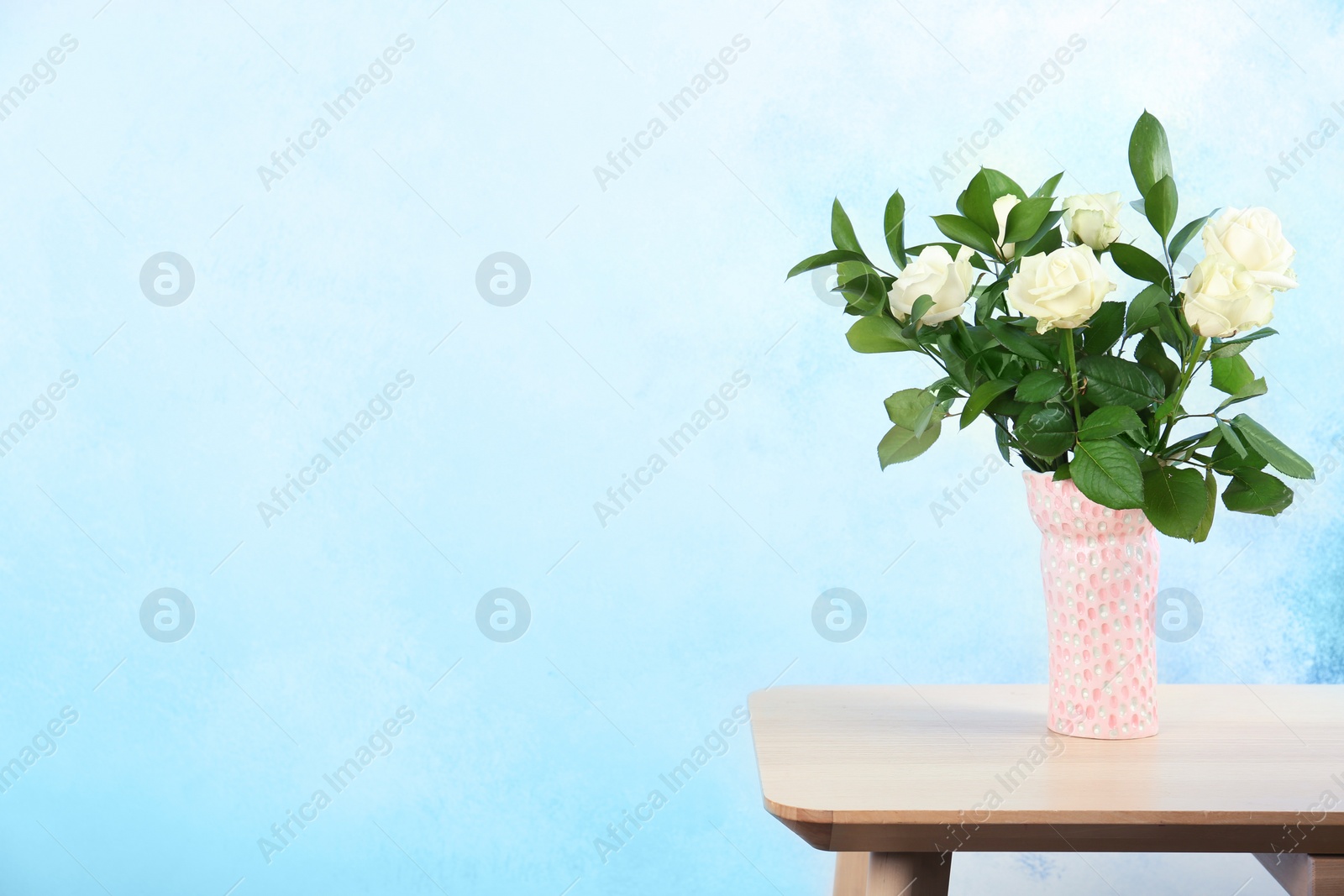 Photo of Vase with bouquet of beautiful roses on table against color background. Space for text