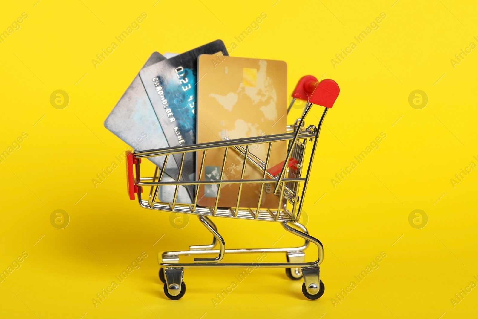 Photo of Small metal shopping cart with credit cards on yellow background