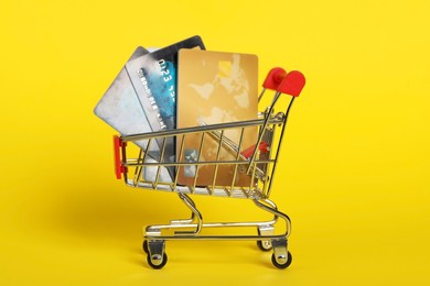 Small metal shopping cart with credit cards on yellow background
