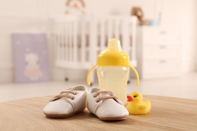 Photo of Baby shoes, bottle and toy duck on wooden table indoors. Maternity leave concept