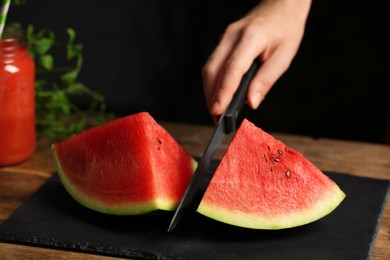 Photo of Woman cutting delicious watermelon on slate board at wooden table, closeup