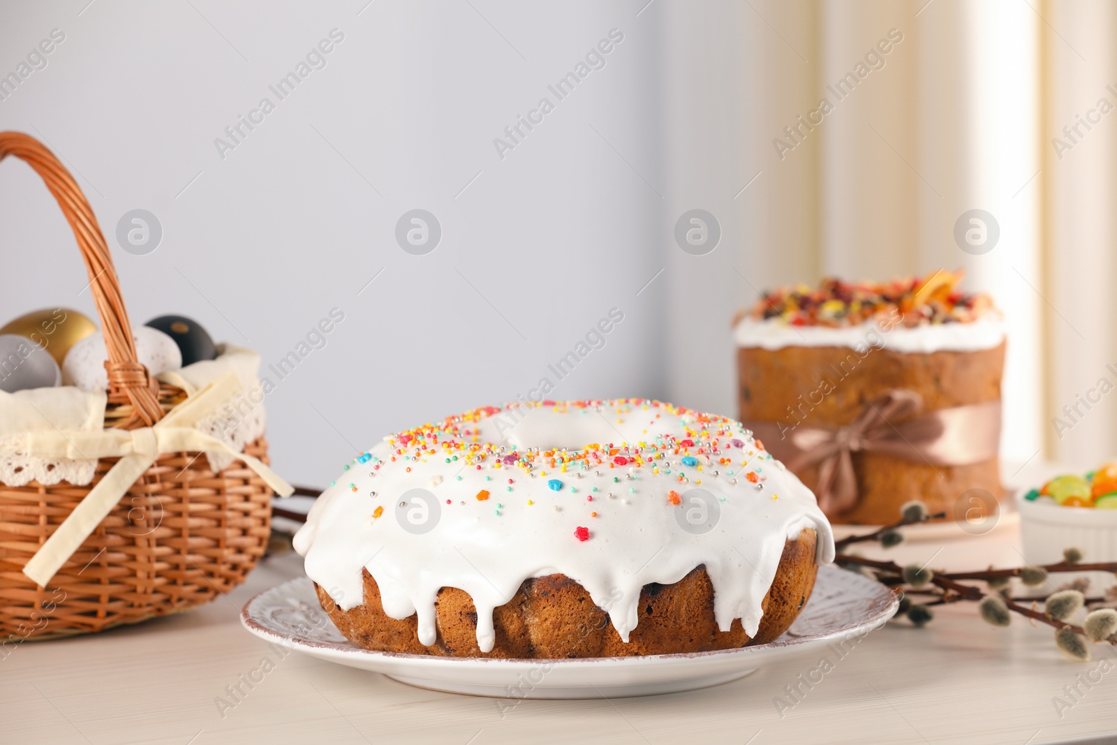 Photo of Delicious Easter cake decorated with sprinkles near willow branches and painted eggs on white wooden table