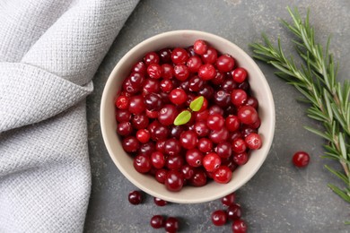 Fresh ripe cranberries in bowl and rosemary on grey table, flat lay