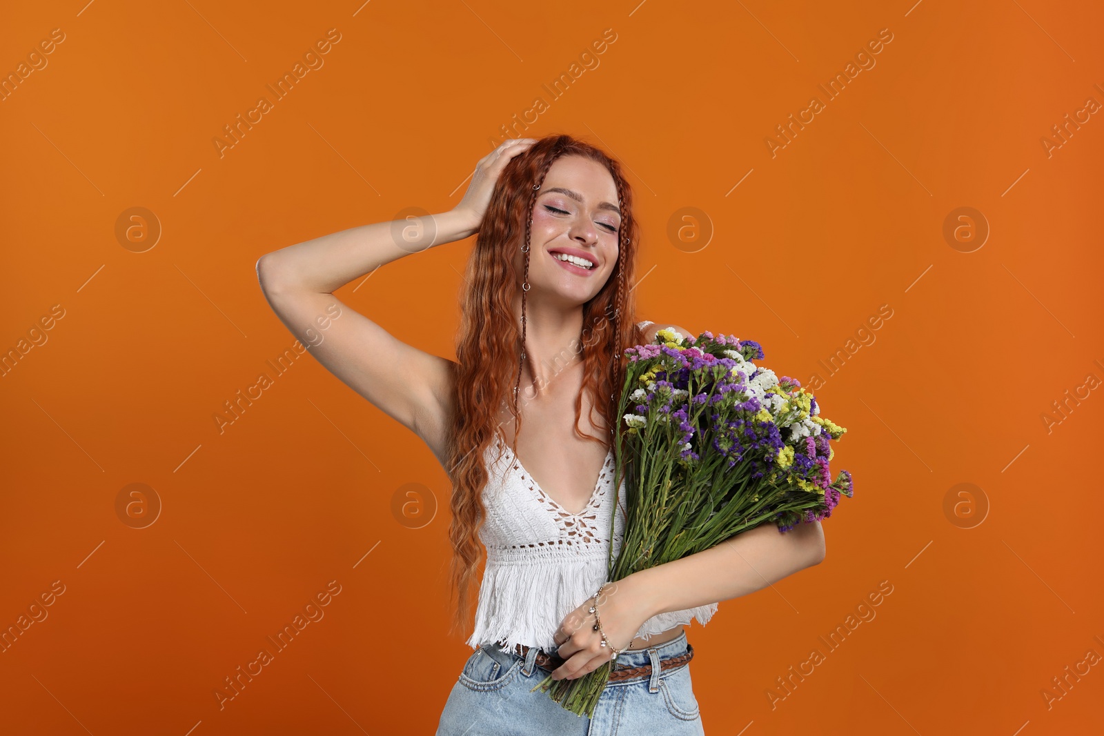 Photo of Beautiful young hippie woman with bouquet of colorful flowers on orange background