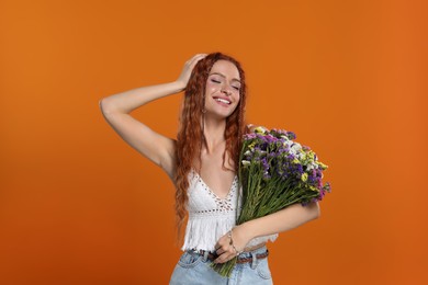 Beautiful young hippie woman with bouquet of colorful flowers on orange background