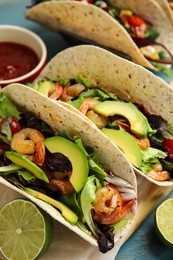 Photo of Delicious tacos with shrimps, avocado and lime on turquoise table, closeup
