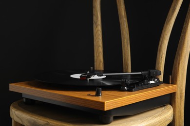 Turntable with vinyl record on wooden chair against black background. Space for text