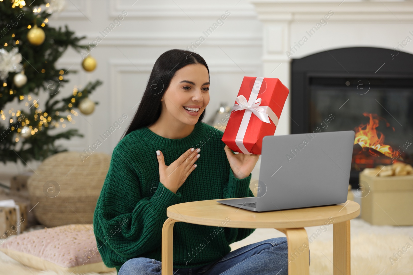 Photo of Celebrating Christmas online with exchanged by mail presents. Smiling woman thanking for gift during video call at home