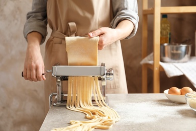 Photo of Young woman preparing noodles with pasta maker at table