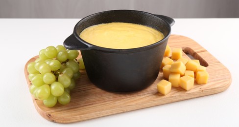 Fondue with tasty melted cheese and grapes on white table