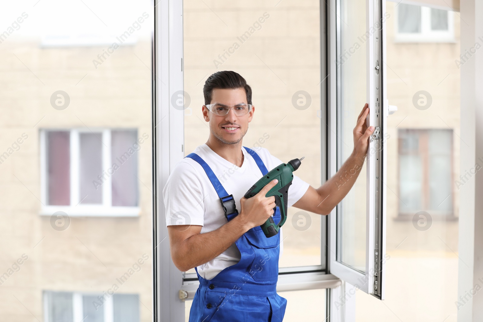 Photo of Construction worker repairing plastic window with electric screwdriver indoors