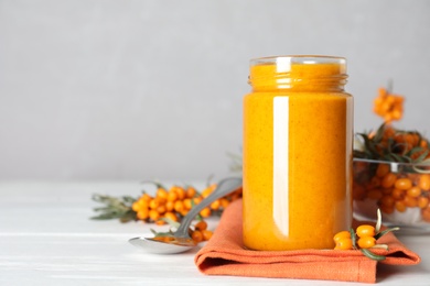 Delicious sea buckthorn jam and fresh berries on white wooden table. Space for text