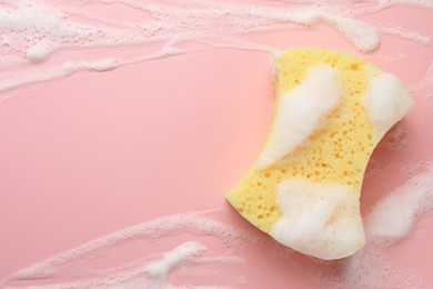 Photo of Yellow sponge with foam on pink background, top view. Space for text