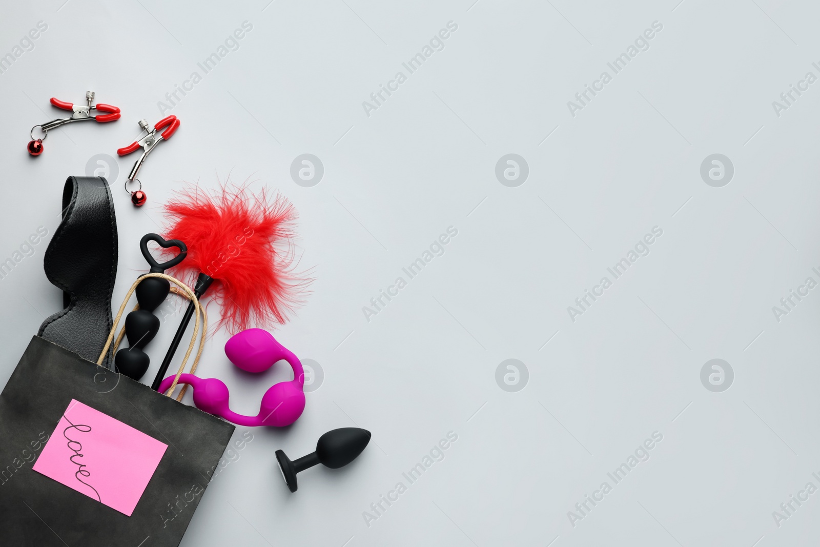 Photo of Paper shopping bag with different sex toys on white background, flat lay. Space for text