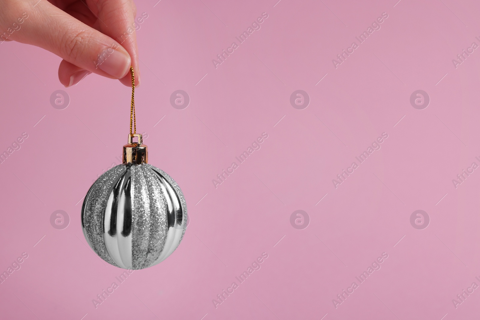 Photo of Woman holding silver Christmas ball on pink background, closeup. Space for text