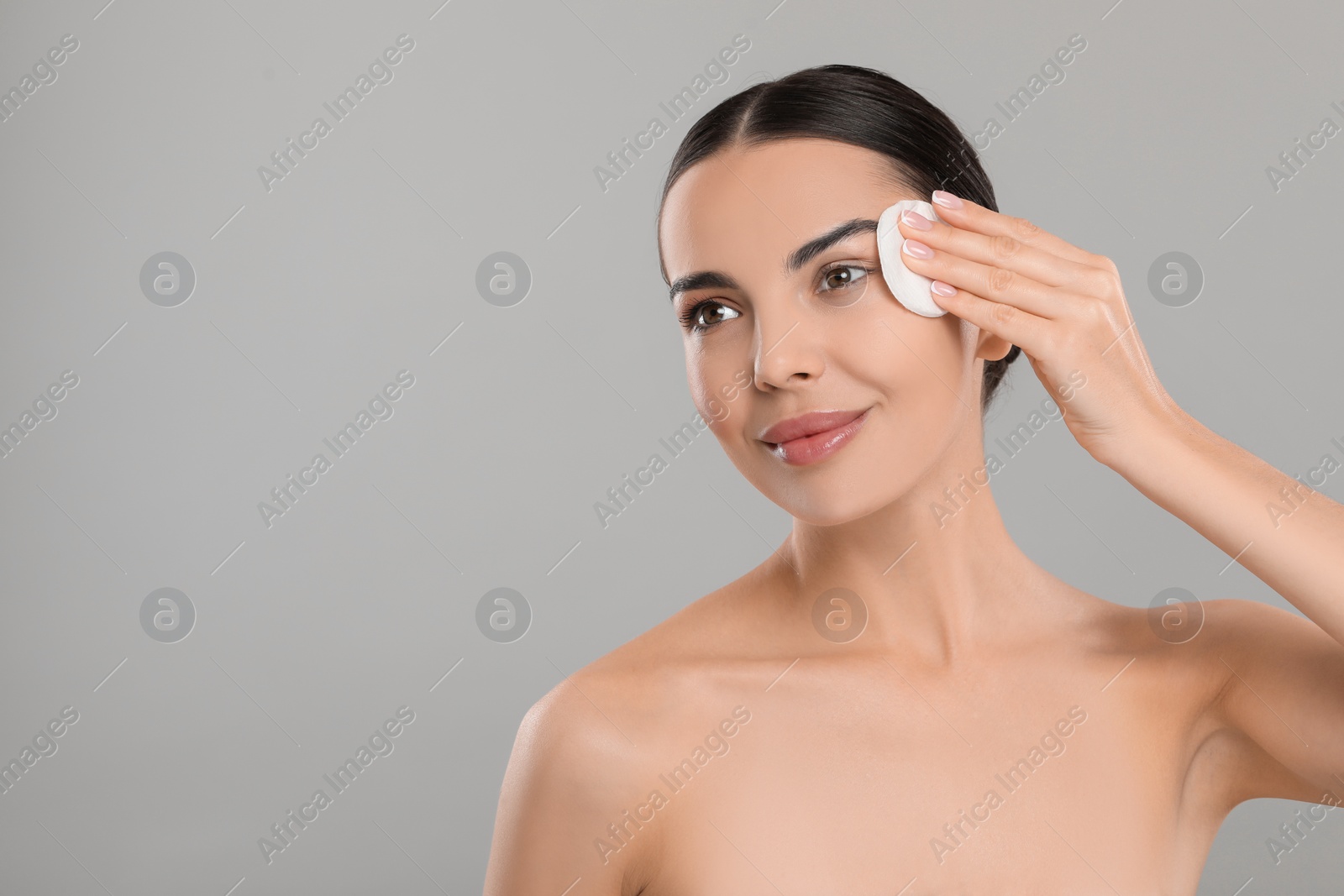 Photo of Beautiful woman removing makeup with cotton pad on light grey background, space for text