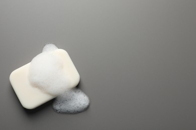 Soap with fluffy foam on grey background, top view. Space for text