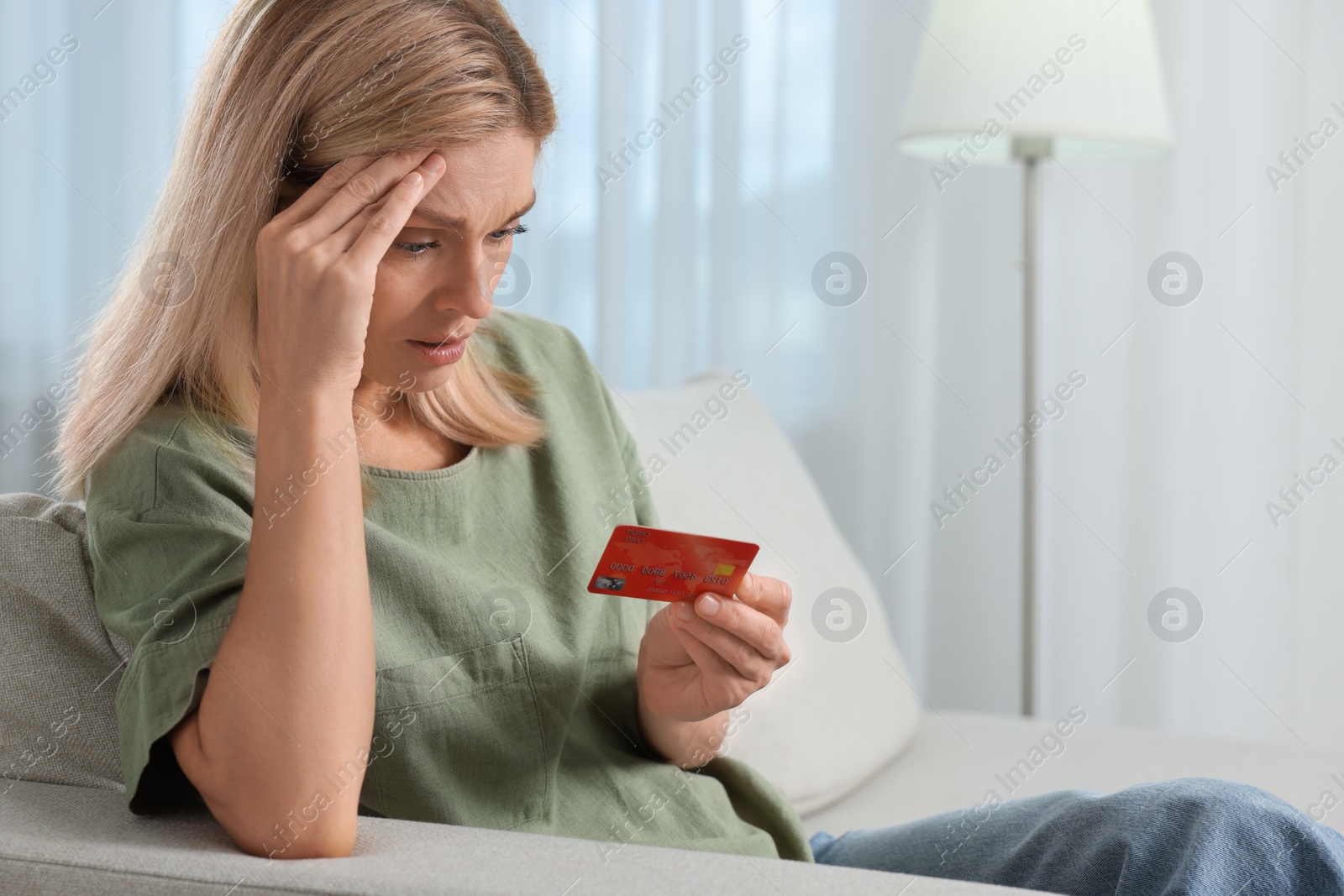 Photo of Stressed woman with credit card on sofa at home. Be careful - fraud