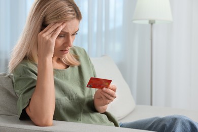 Stressed woman with credit card on sofa at home. Be careful - fraud
