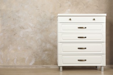 Photo of Modern chest of drawers near beige wall. Space for text