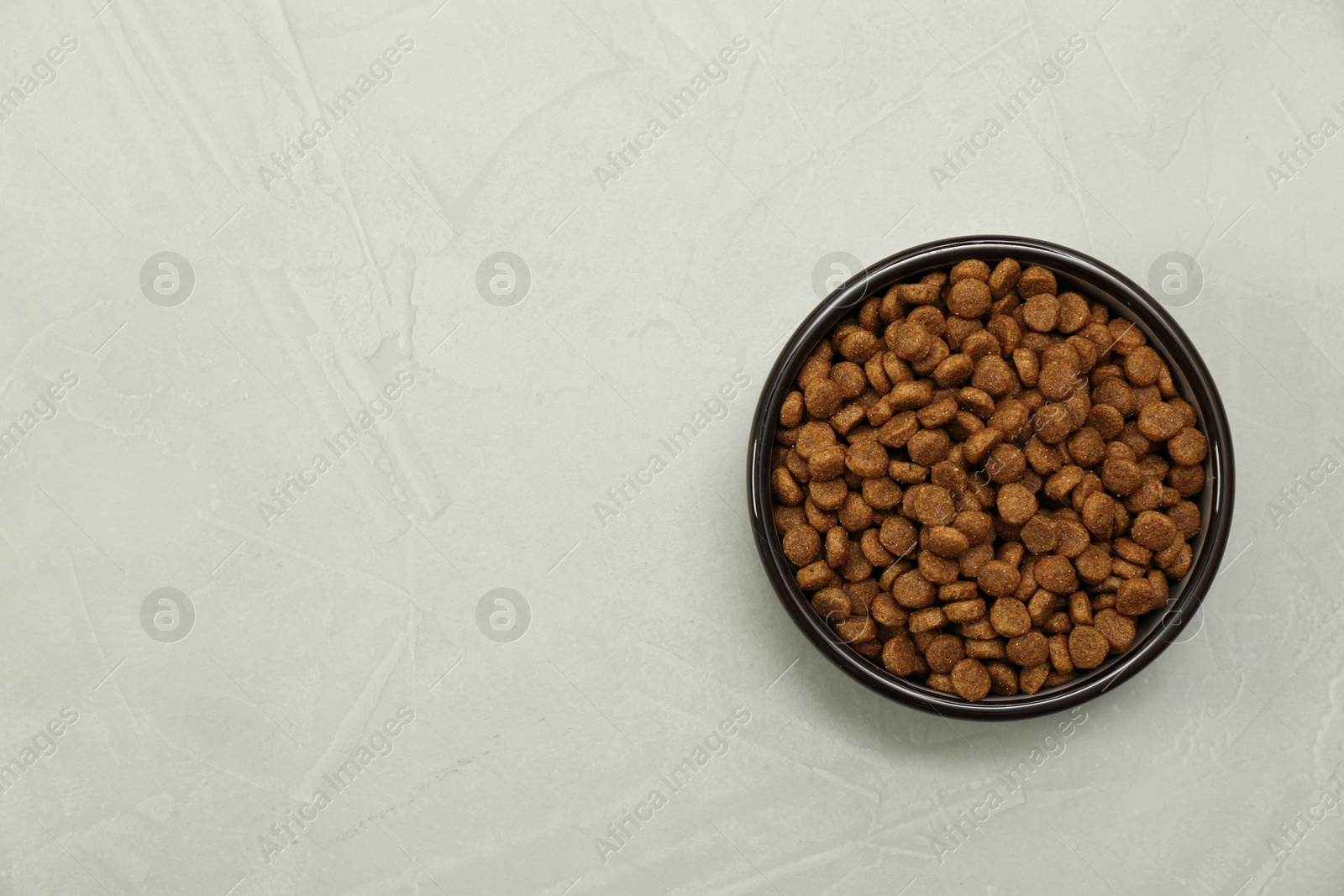 Photo of Dry food in pet bowl on grey background, top view. Space for text