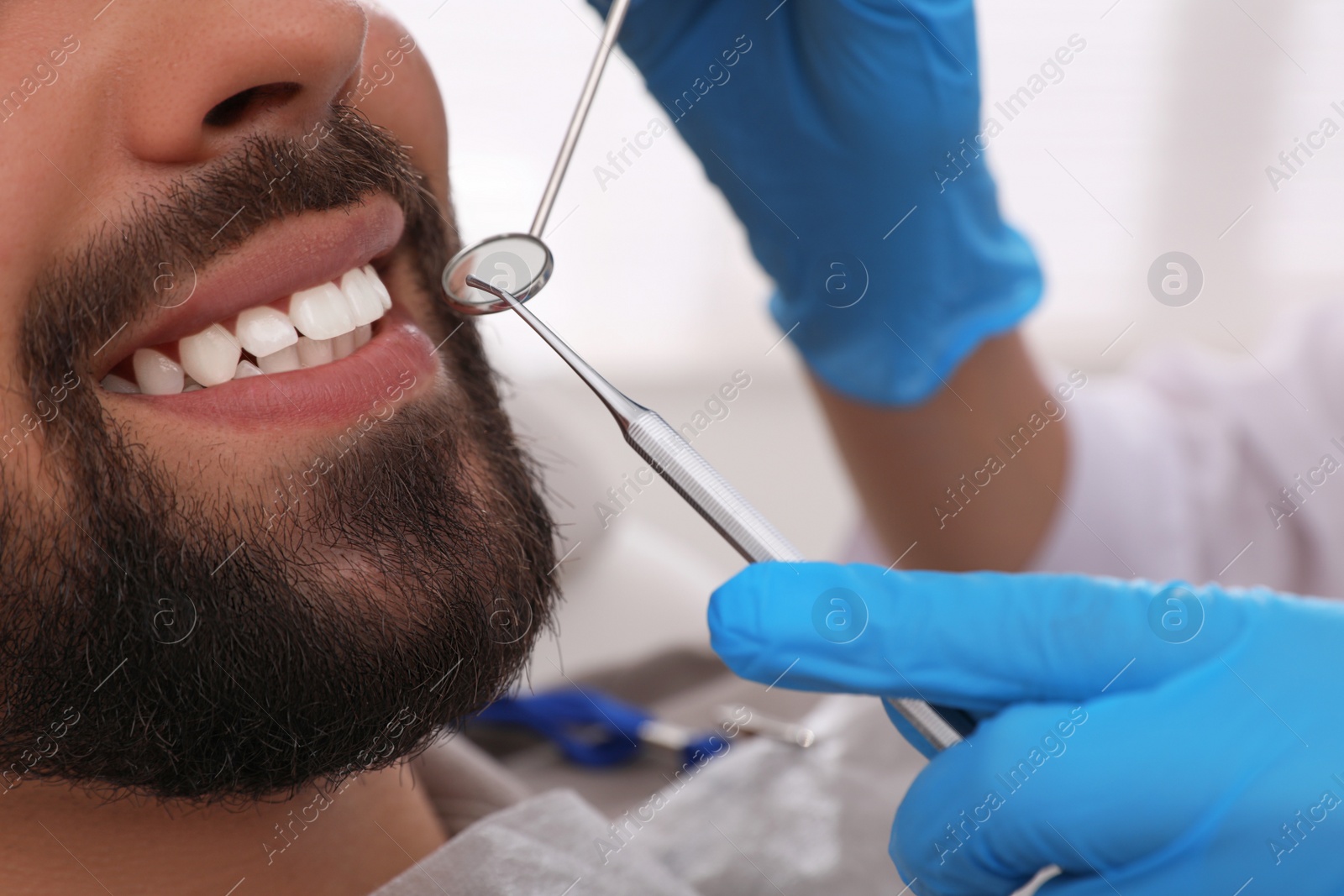 Photo of Dentist examining young man's teeth in clinic, closeup