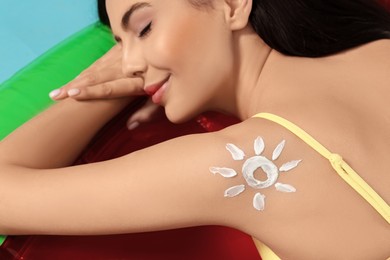 Photo of Young woman with sun protection cream on inflatable mattress against light blue background, closeup