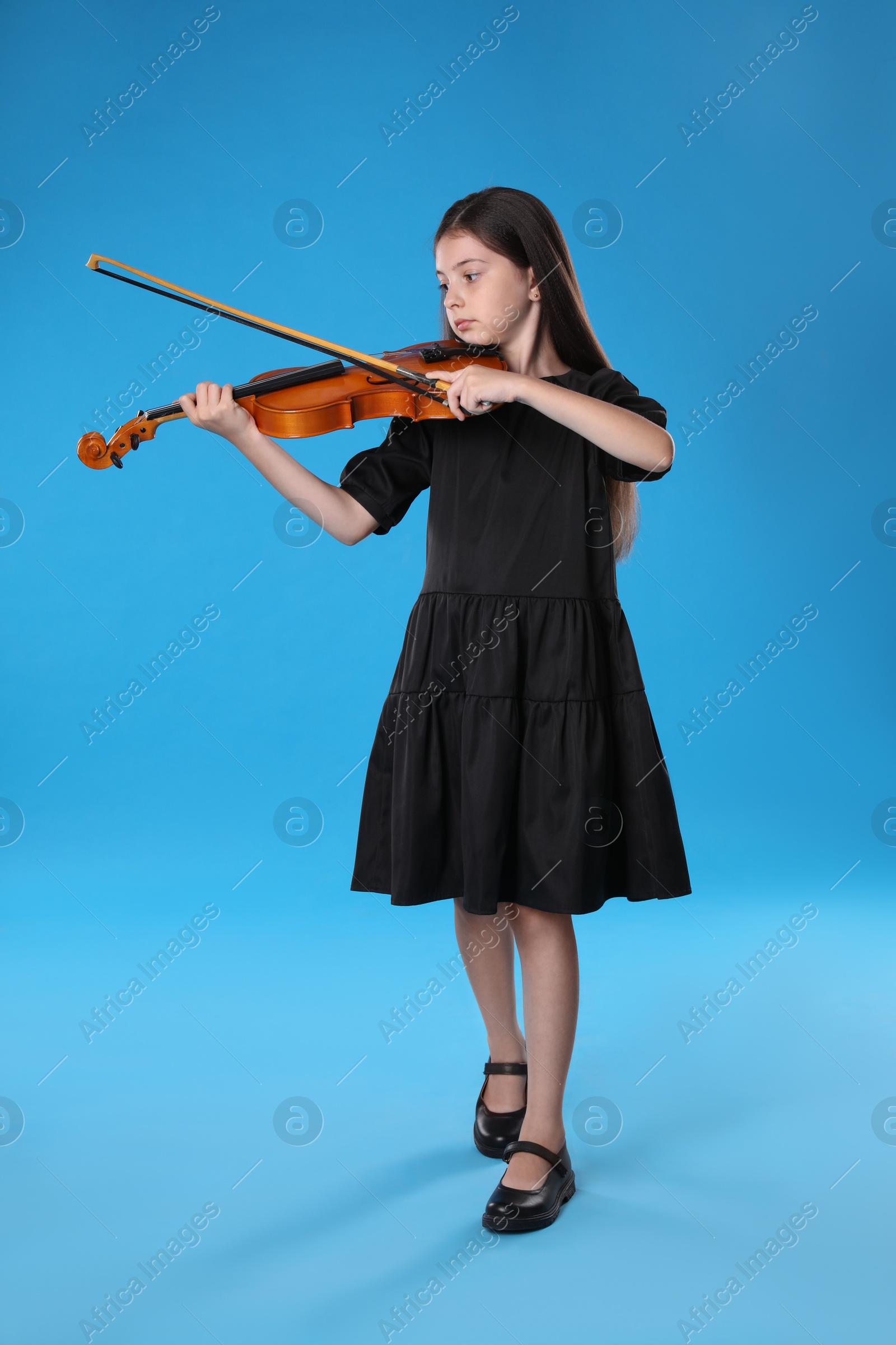 Photo of Preteen girl playing violin on light blue background